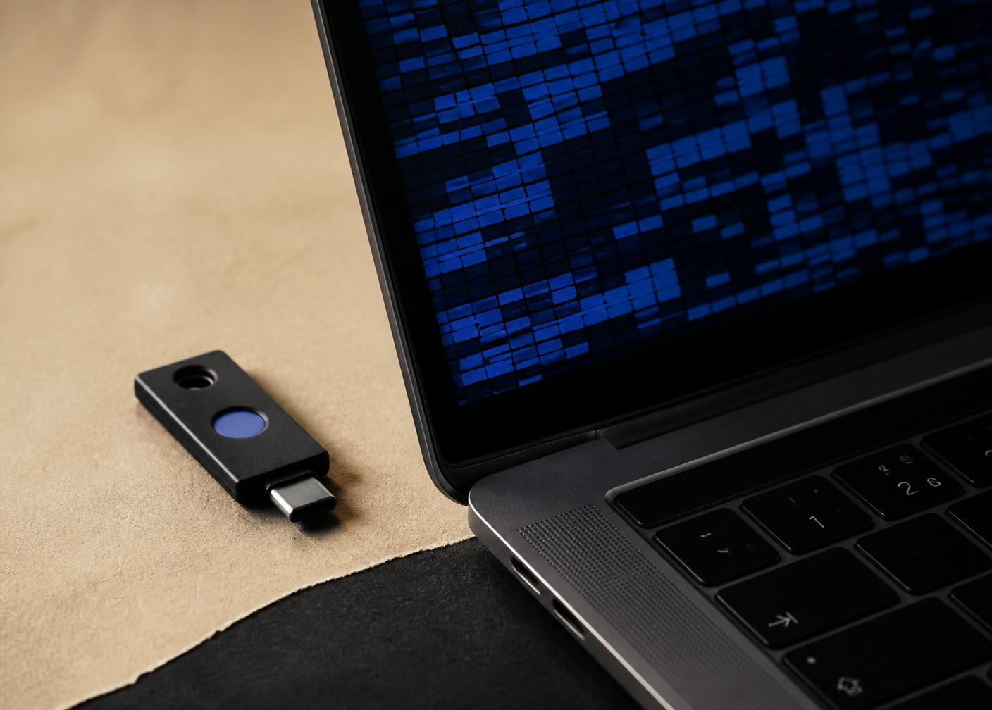 A hardware security key resting beside a laptop screen showing abstract blue encrypted data blocks
